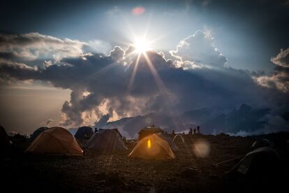 tentes-de-multiples-couleurs-sur-sol-rocheux-avec-soleil-qui-perce-les-nuages-en-fond